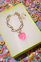 Gold bracelet with a pink heart charm on a colorful background