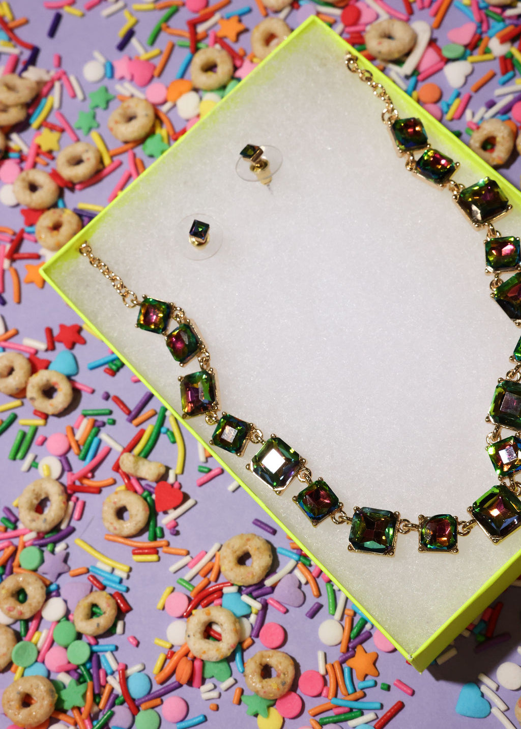 Necklace with colorful gemstones on a box surrounded by cereal and sprinkles