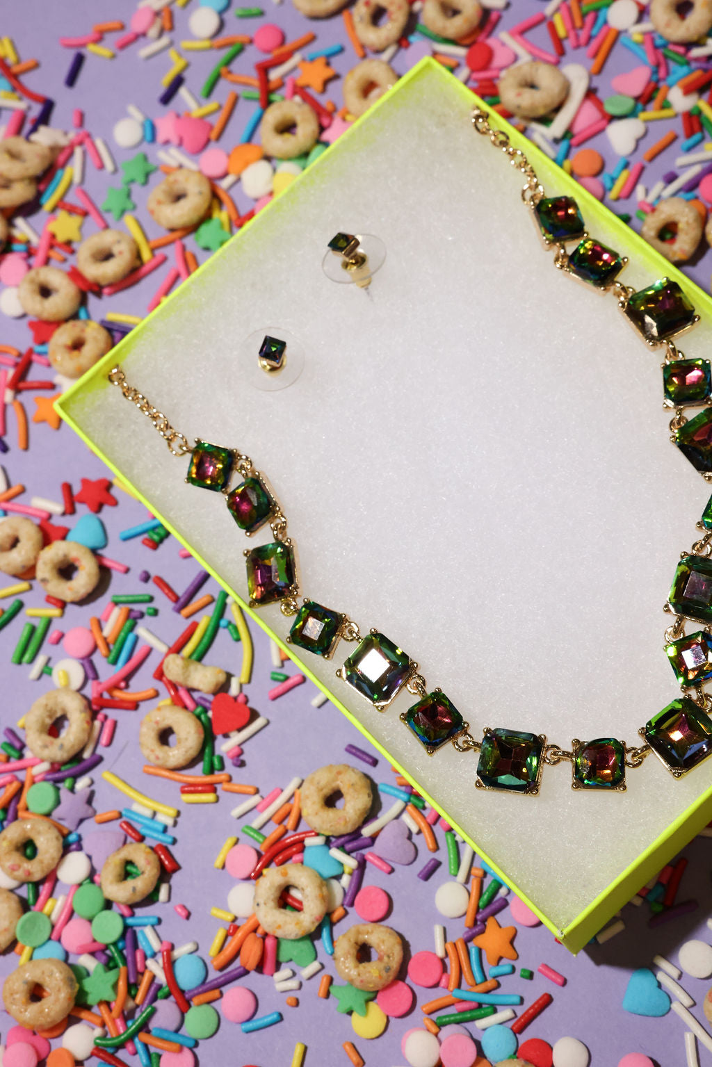 Necklace with colorful gemstones on a box surrounded by cereal and sprinkles