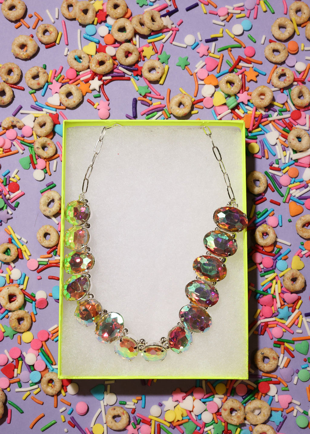 Necklace in a box surrounded by colorful cereal and sprinkles on a purple background