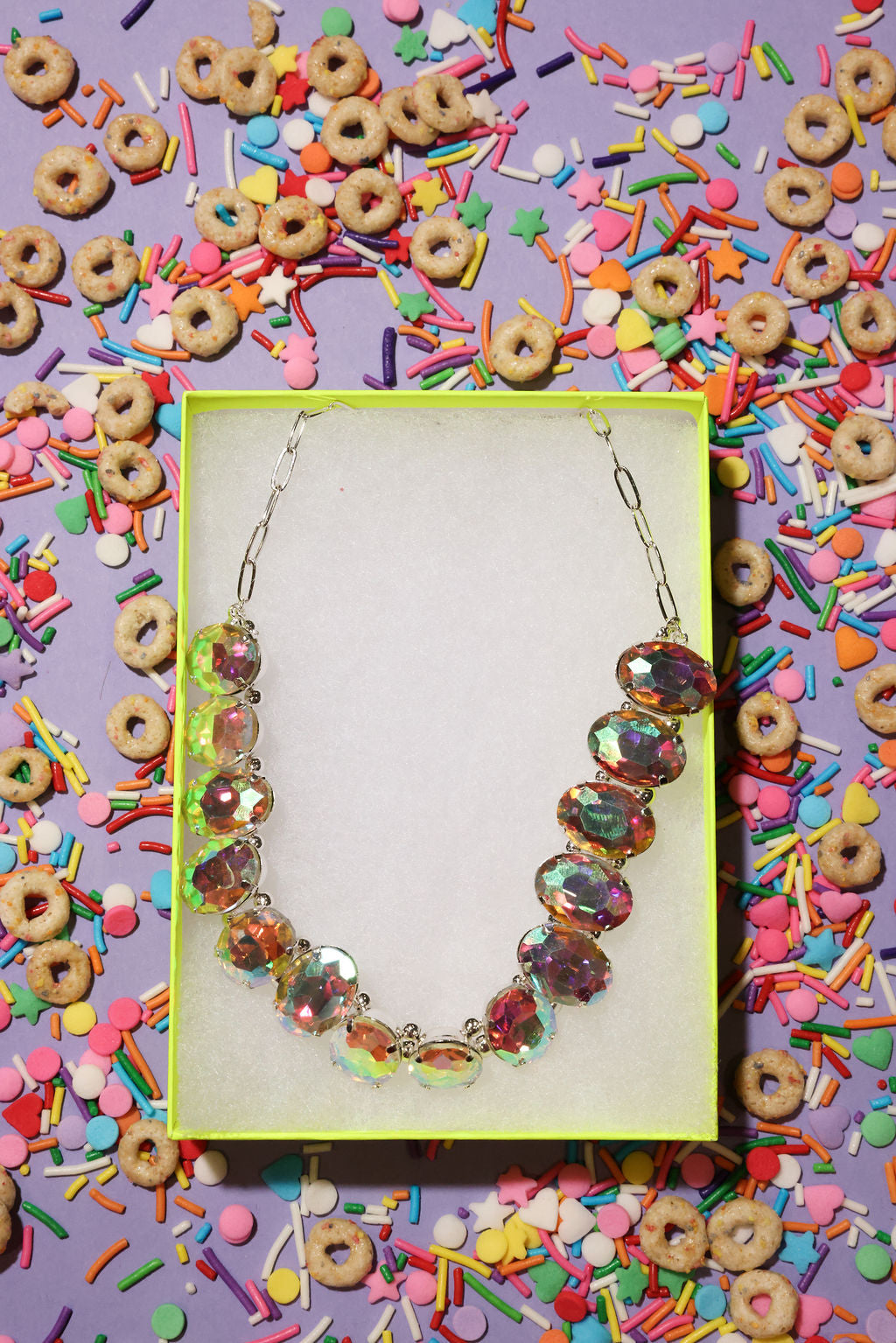 Necklace in a box surrounded by colorful cereal and sprinkles on a purple background