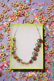 Necklace in a box surrounded by colorful cereal and sprinkles on a purple background