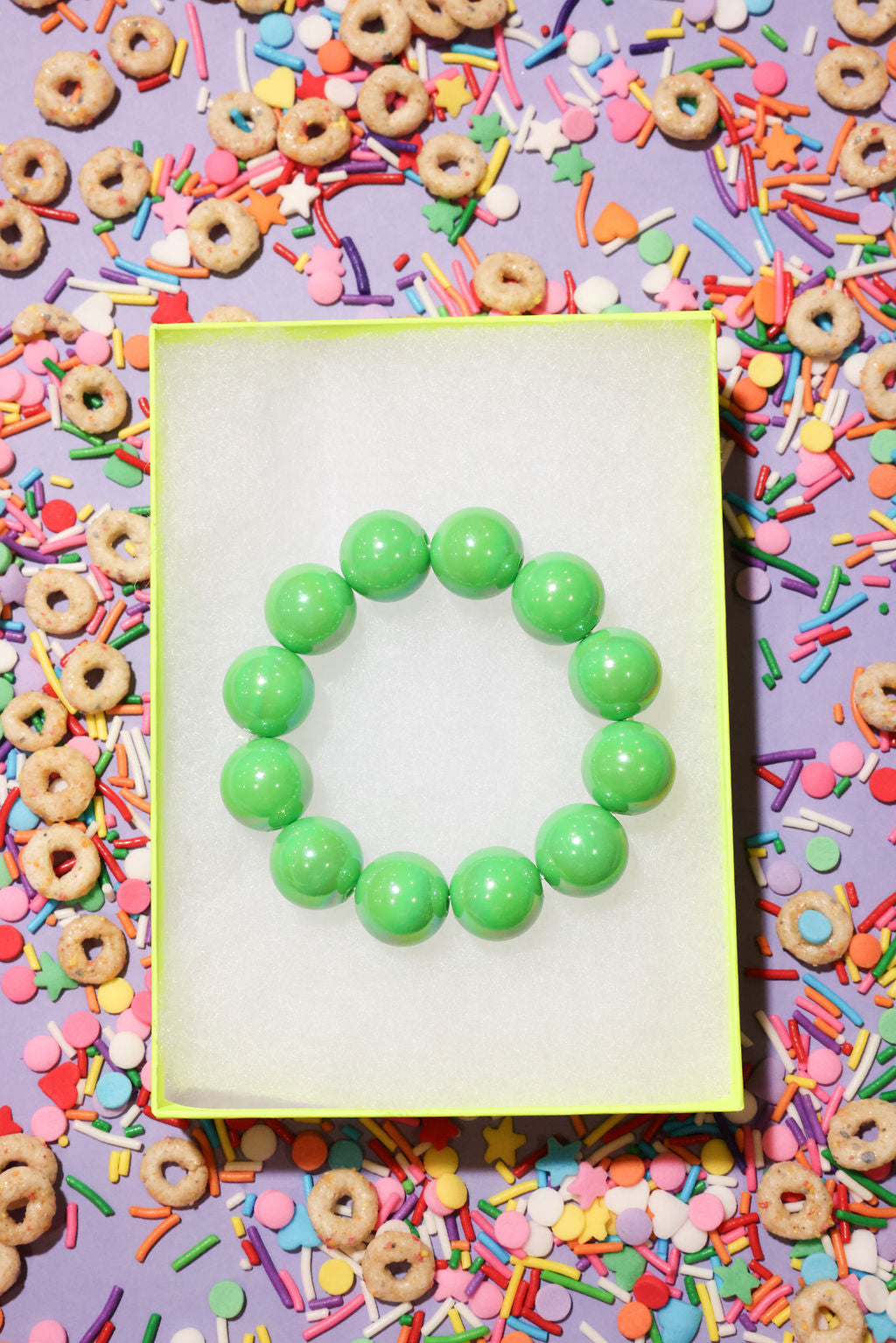 Green bracelet on a white card with colorful cereal and sprinkles in the background