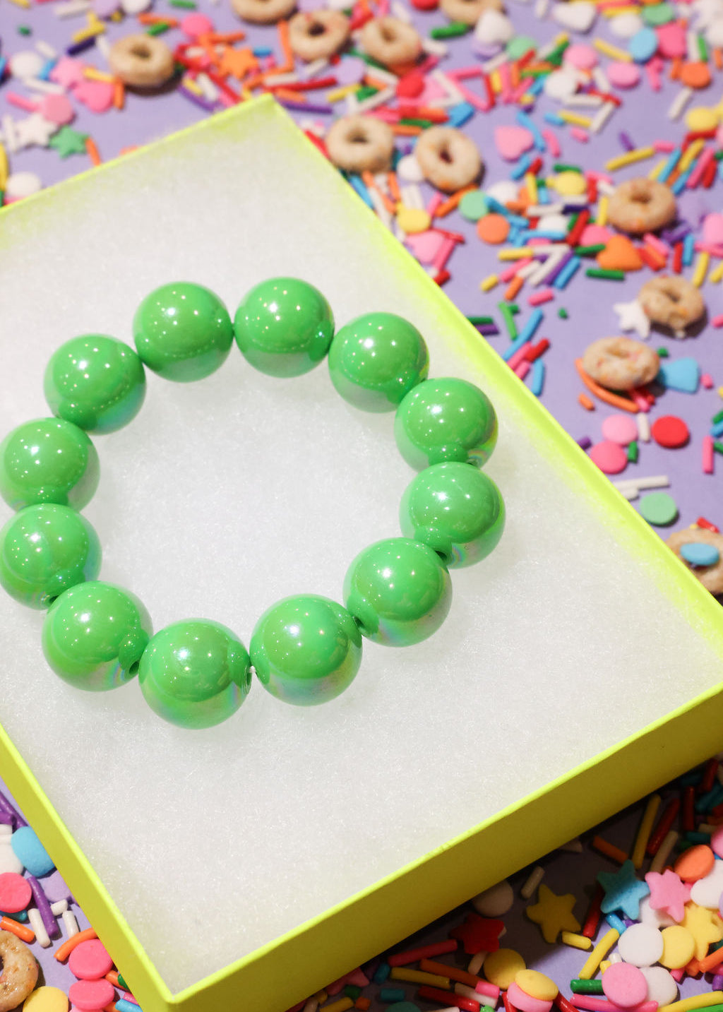 Green beaded bracelet on a yellow stand with colorful sprinkles in the background
