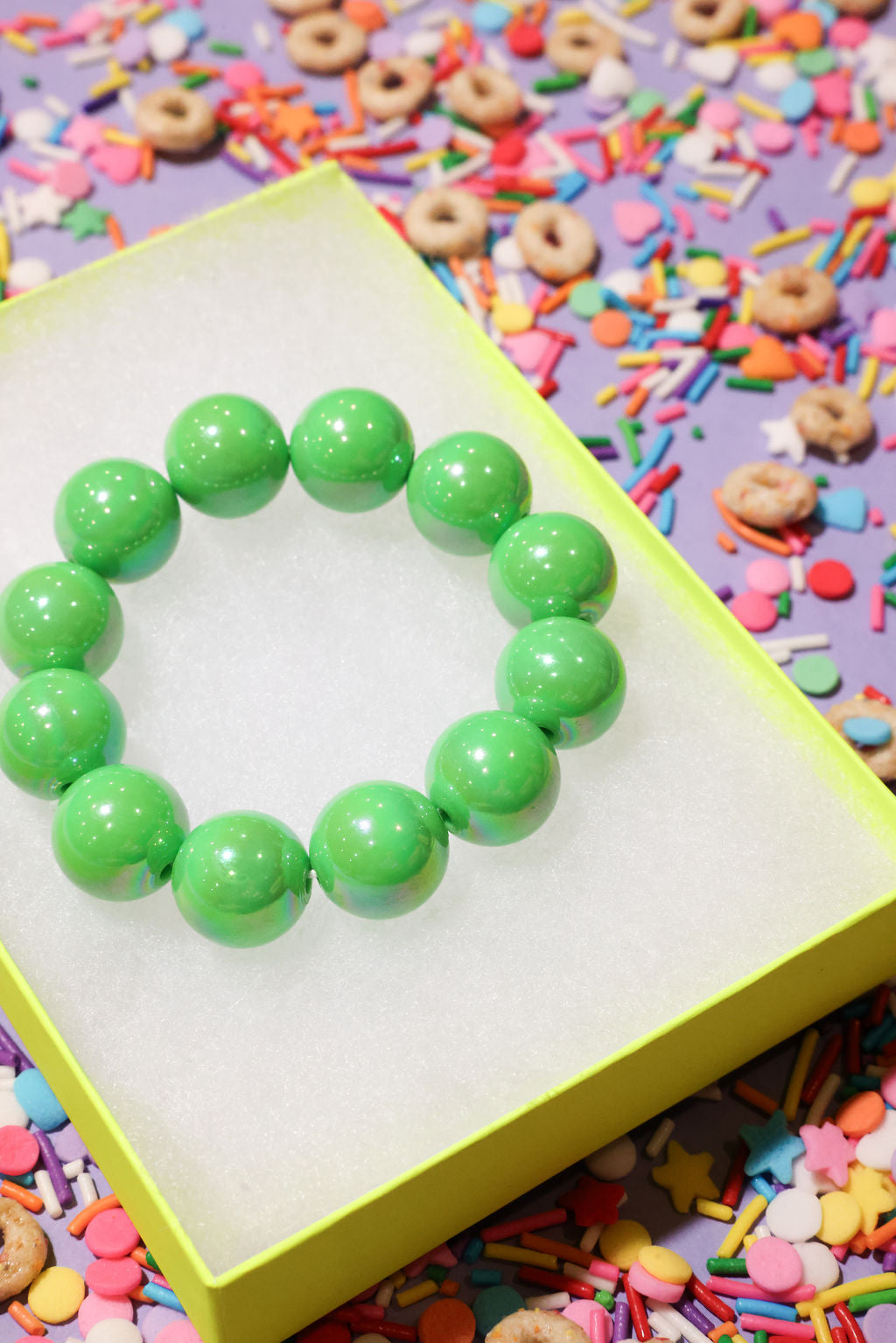 Green beaded bracelet on a yellow stand with colorful sprinkles in the background