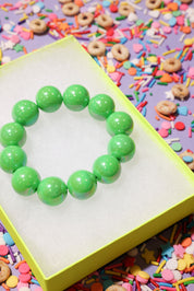 Green beaded bracelet on a yellow stand with colorful sprinkles in the background