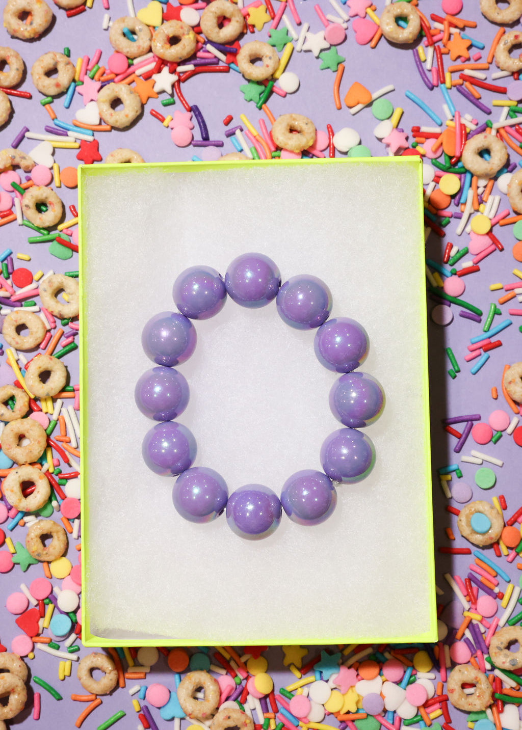 Purple beaded bracelet on a white card with colorful cereal and sprinkles in the background