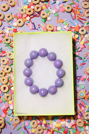 Purple beaded bracelet on a white card with colorful cereal and sprinkles in the background