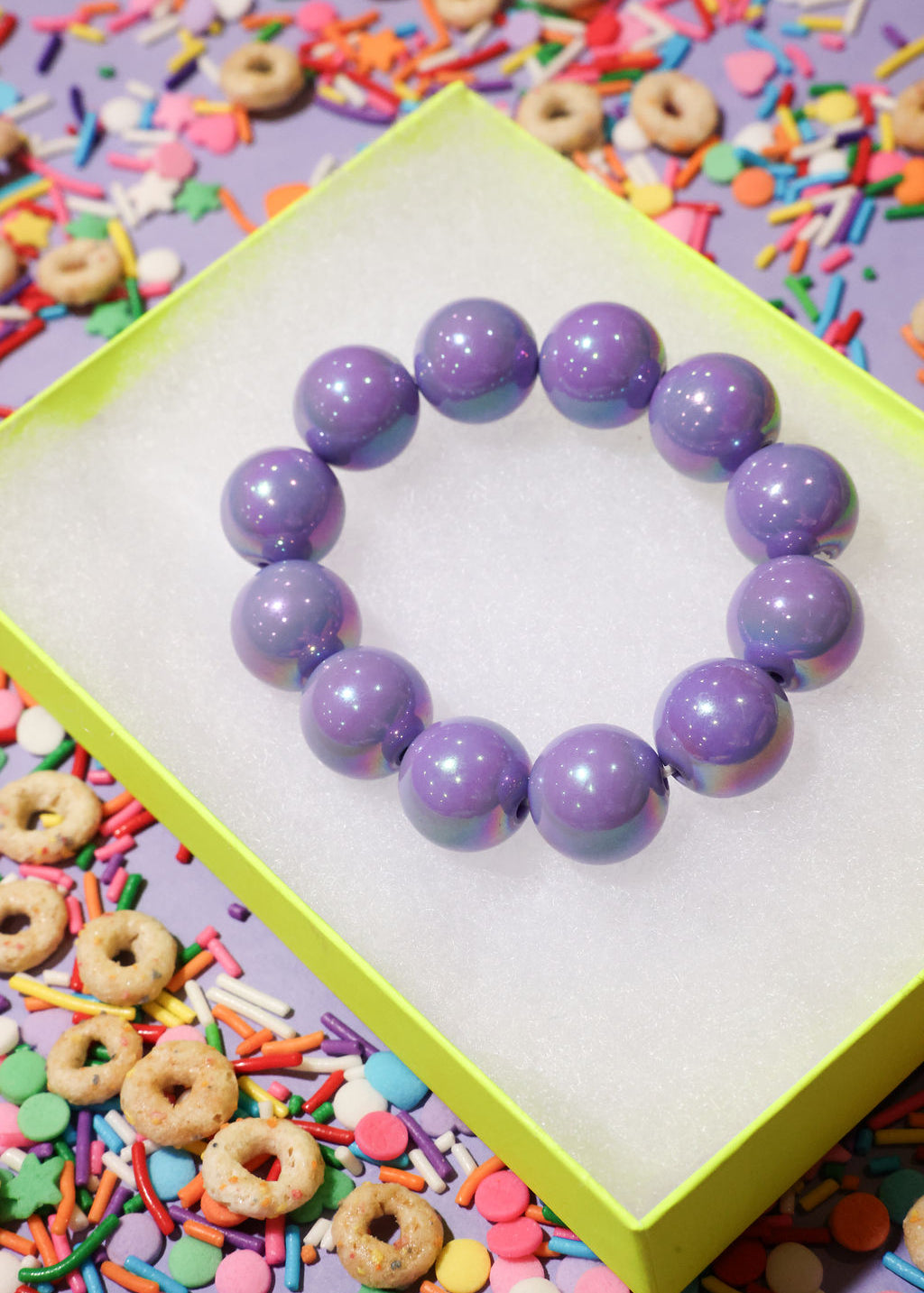 Purple beaded bracelet on a white card with colorful sprinkles and cookies in the background