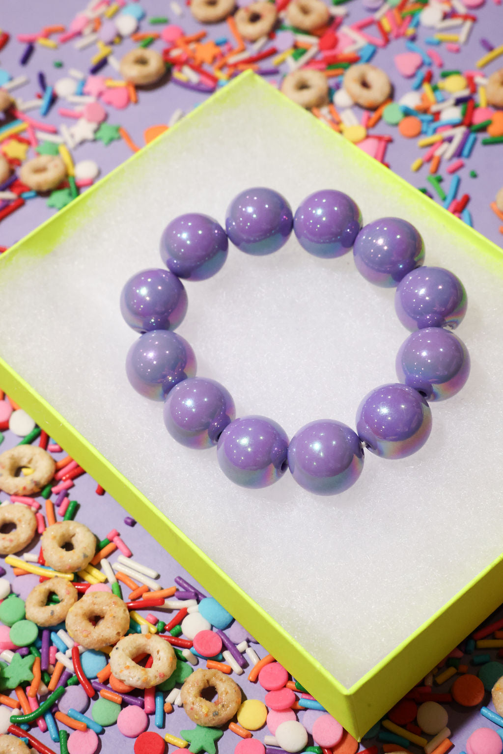 Purple beaded bracelet on a white card with colorful sprinkles and cookies in the background