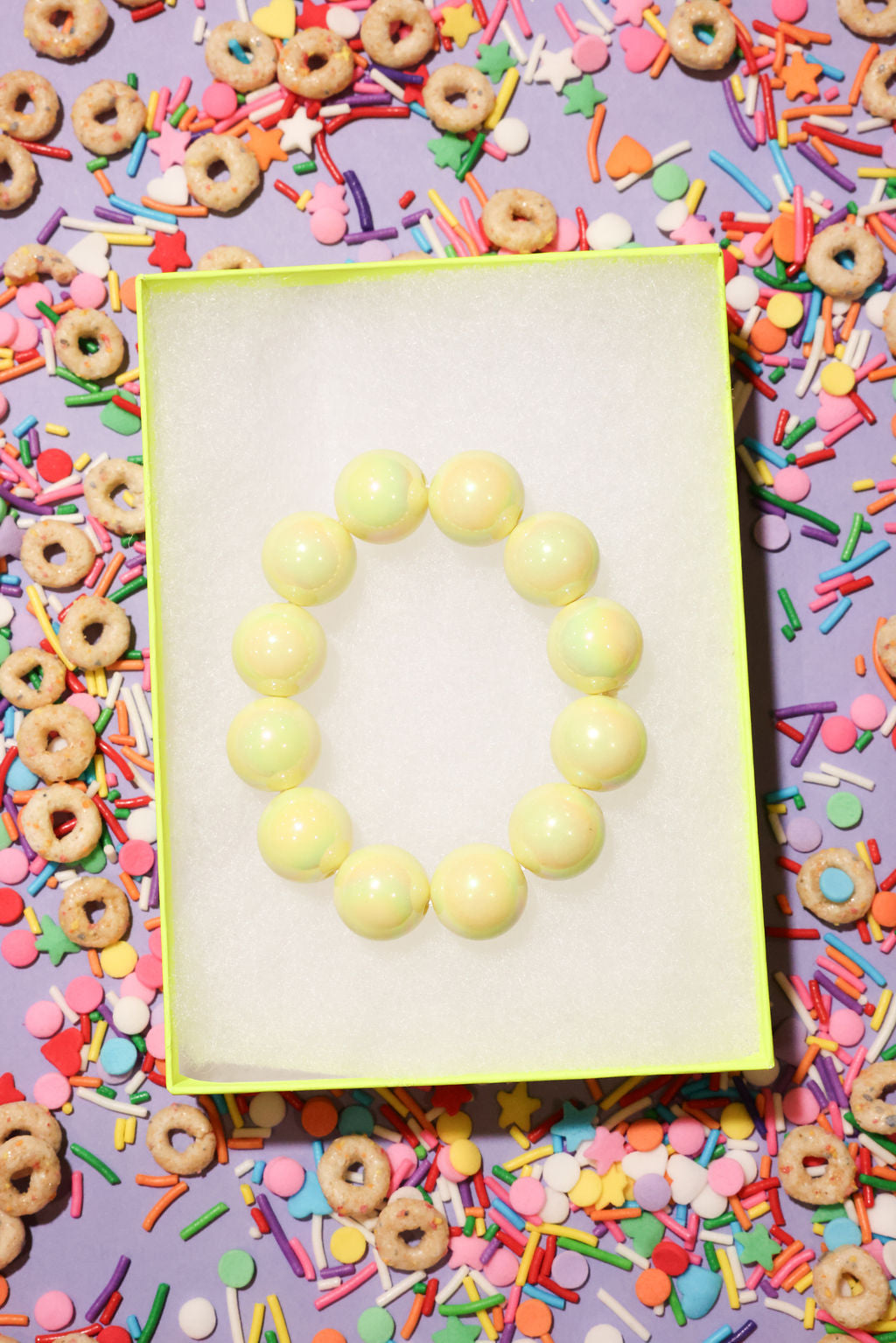 Yellow beaded bracelet on a white card surrounded by colorful cereal and sprinkles on a purple background