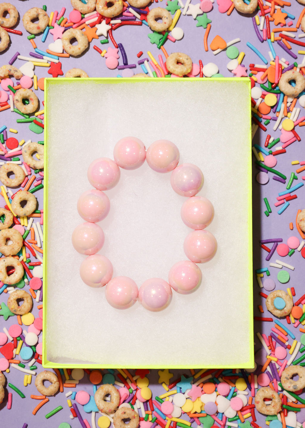 Pink beaded bracelet on a white card surrounded by colorful cereal and sprinkles
