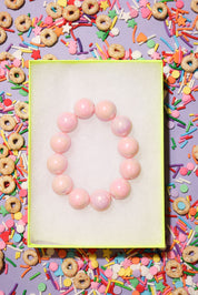 Pink beaded bracelet on a white card surrounded by colorful cereal and sprinkles