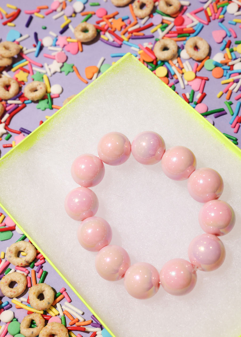 Pink beaded bracelet on a white surface with colorful sprinkles and donuts in the background