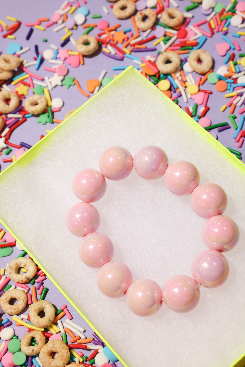 Pink beaded bracelet on a white surface with colorful sprinkles and donuts in the background