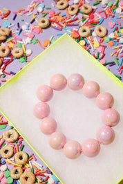 Pink beaded bracelet on a white surface with colorful sprinkles and donuts in the background