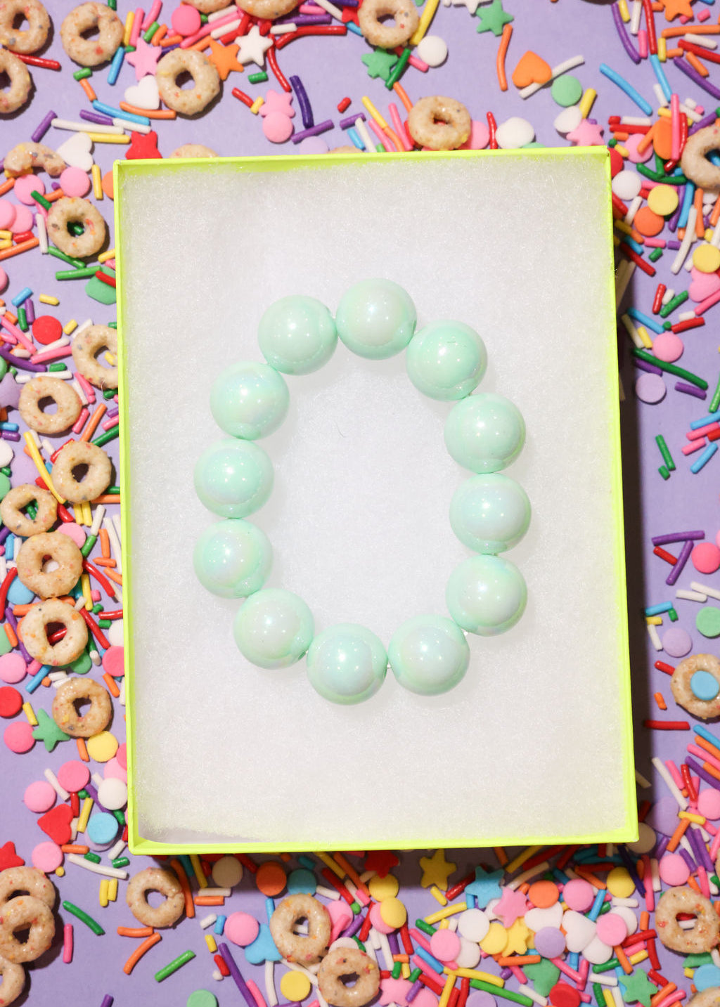 Green bracelet on a white card with colorful cereal and sprinkles in the background