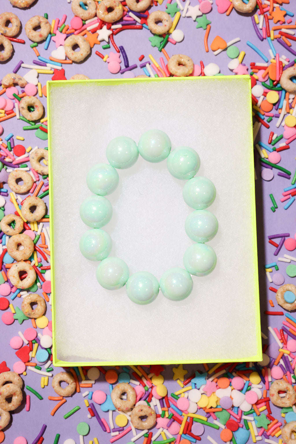 Green bracelet on a white card with colorful cereal and sprinkles in the background