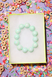 Green bracelet on a white card with colorful cereal and sprinkles in the background