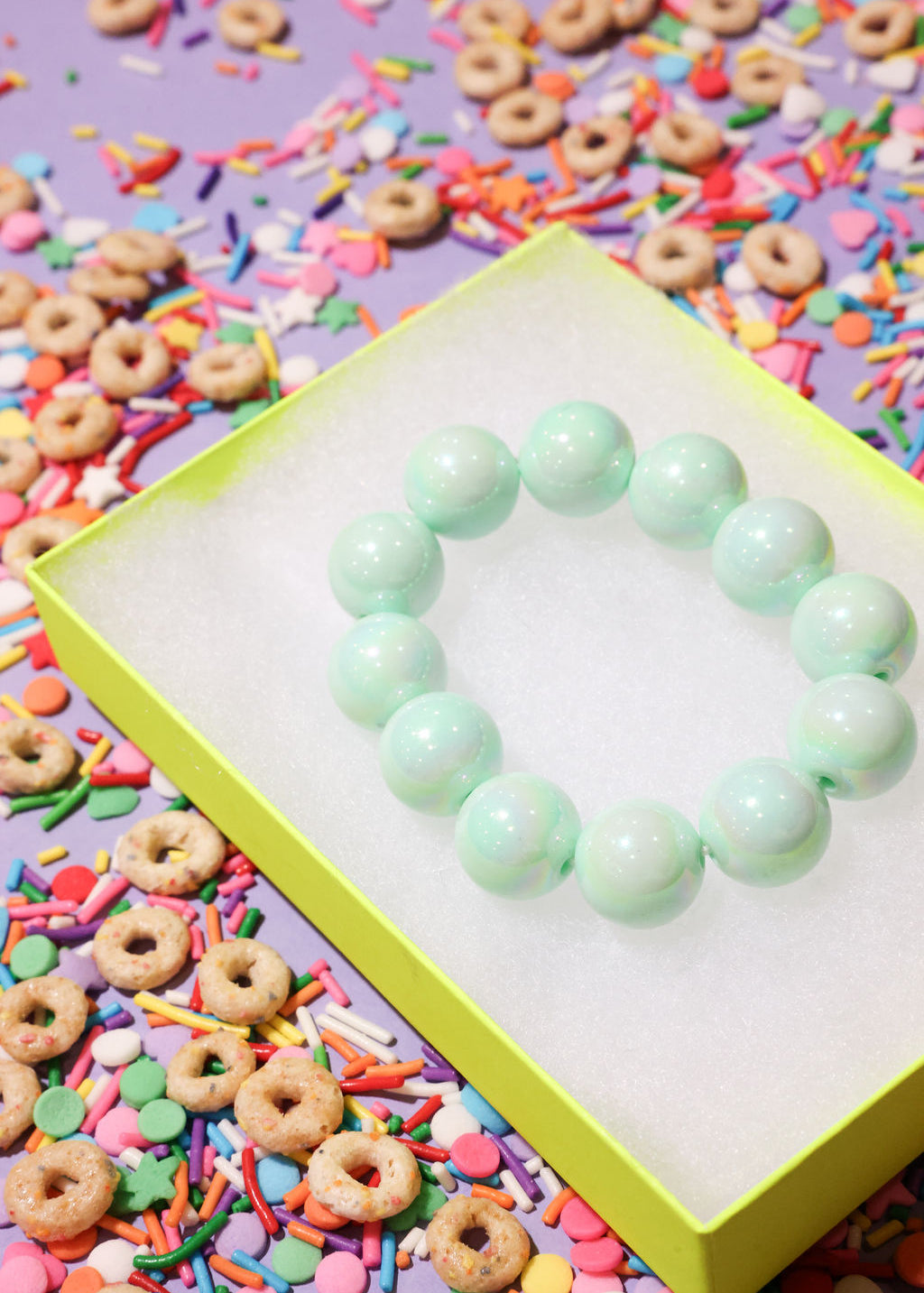 Light green beaded bracelet on a colorful background with sprinkles and donuts.
