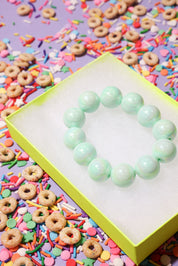 Light green beaded bracelet on a colorful background with sprinkles and donuts.