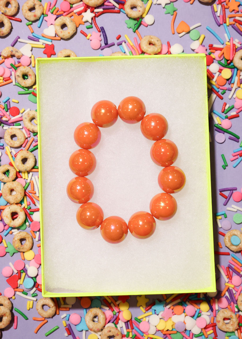 Orange beaded bracelet on a white card with colorful cereal and sprinkles in the background