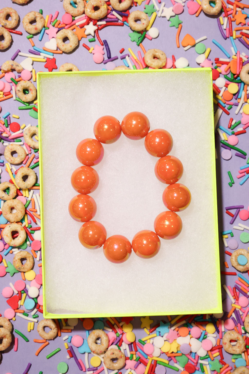 Orange beaded bracelet on a white card with colorful cereal and sprinkles in the background