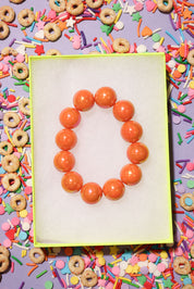 Orange beaded bracelet on a white card with colorful cereal and sprinkles in the background