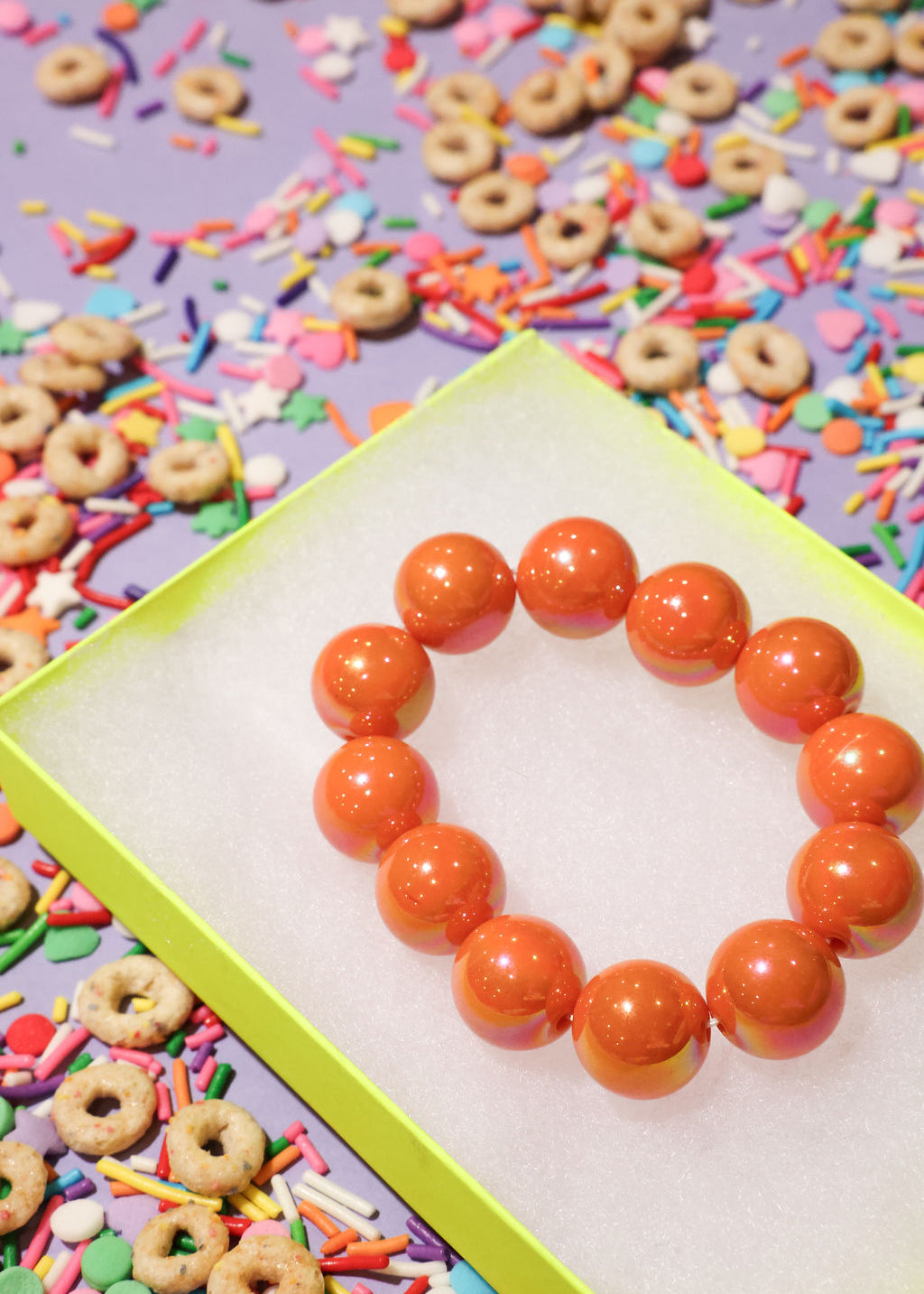 Orange beaded bracelet on a colorful background with sprinkles and donut-shaped cereal