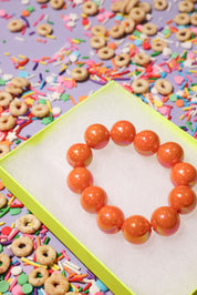Orange beaded bracelet on a colorful background with sprinkles and donut-shaped cereal