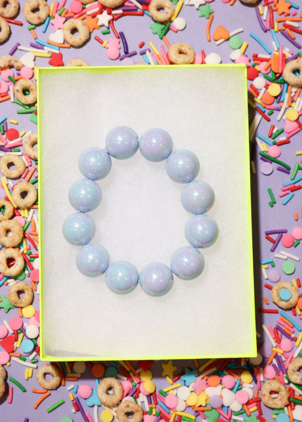 Light blue beaded bracelet on a yellow card with colorful cereal and sprinkles in the background