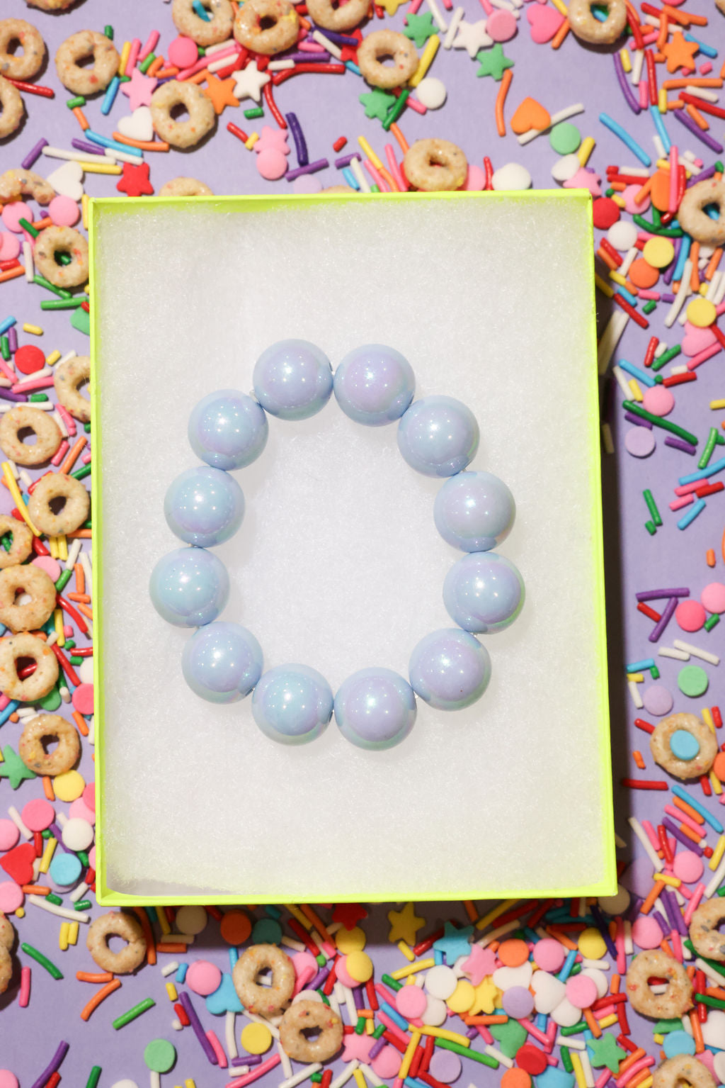 Light blue beaded bracelet on a yellow card with colorful cereal and sprinkles in the background
