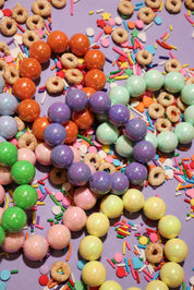 Colorful beaded bracelets and sprinkles on a purple background