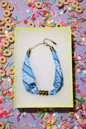 Blue bandana bracelet with gold accents in a box surrounded by colorful cereal and sprinkles.