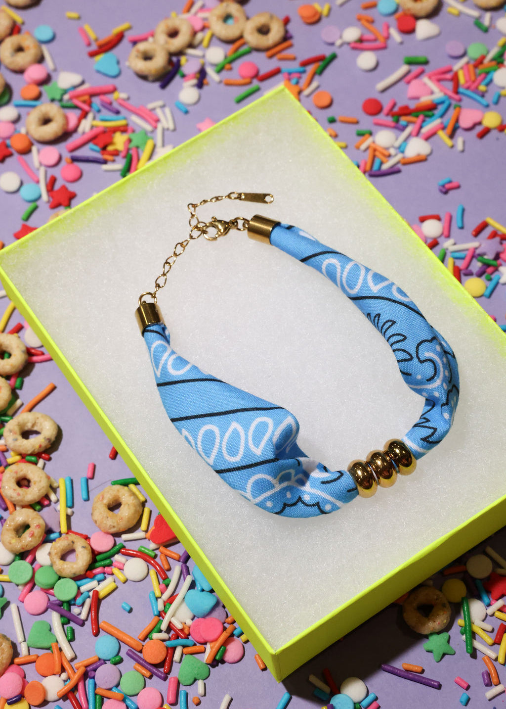 Blue beaded bandana bracelet with gold accents on a colorful sprinkles background