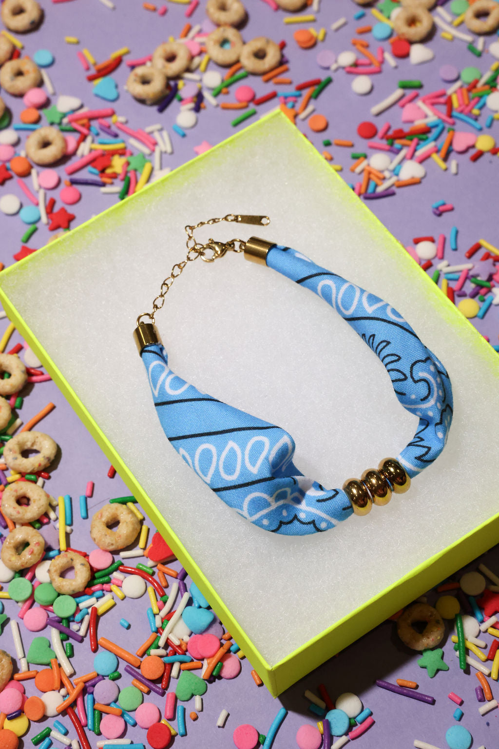 Blue beaded bandana bracelet with gold accents on a colorful sprinkles background