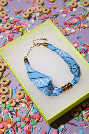 Blue beaded bandana bracelet with gold accents on a colorful sprinkles background