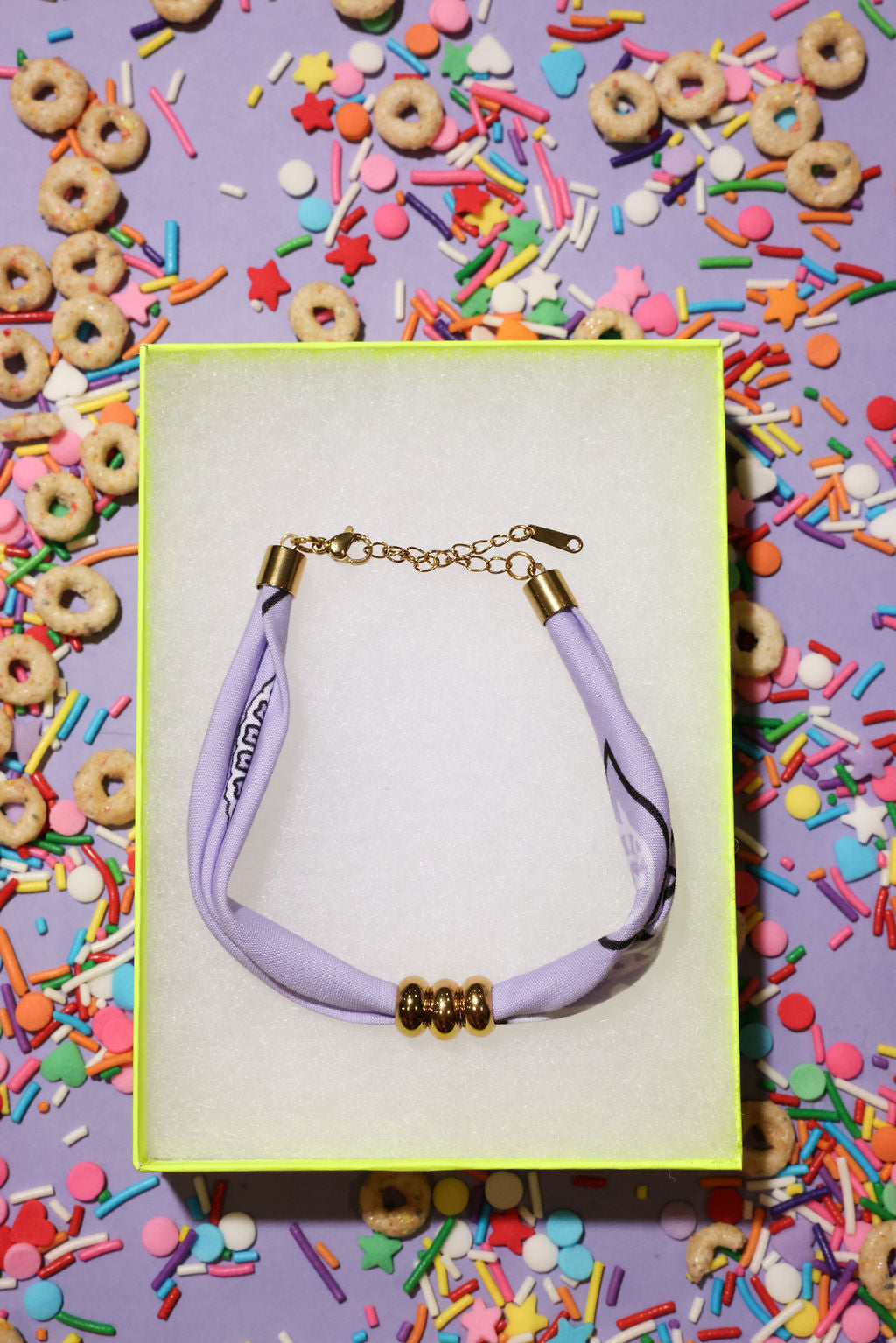 bracelet with a purple bandana cord and gold clasp on a colorful background with donuts and sprinkles