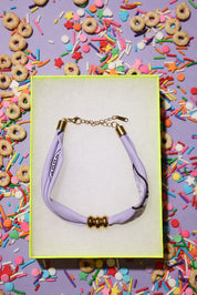 bracelet with a purple bandana cord and gold clasp on a colorful background with donuts and sprinkles