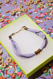Lavender bracelet with gold accents on a yellow box surrounded by colorful cereal and sprinkles