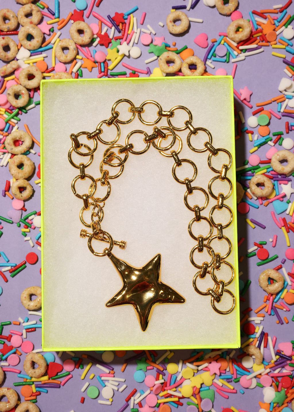 Gold necklace with a star charm in a box surrounded by colorful cereal and sprinkles.