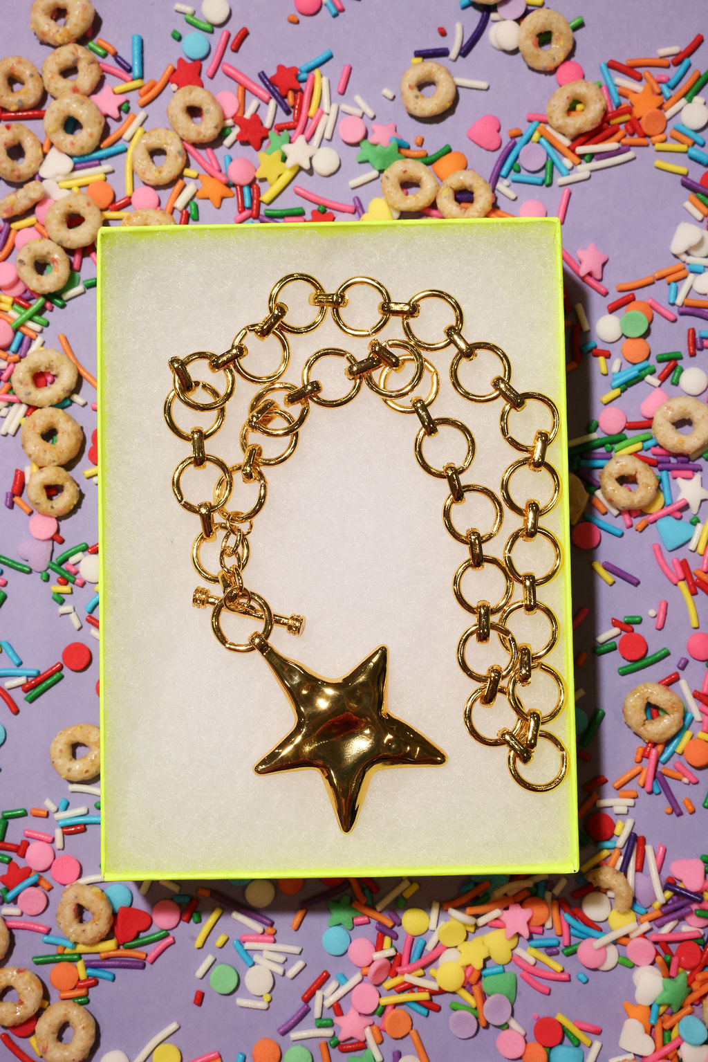 Gold necklace with a star charm in a box surrounded by colorful cereal and sprinkles.