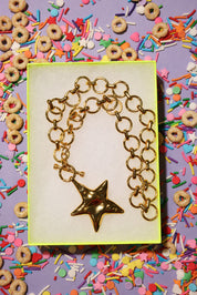 Gold necklace with a star charm in a box surrounded by colorful cereal and sprinkles.