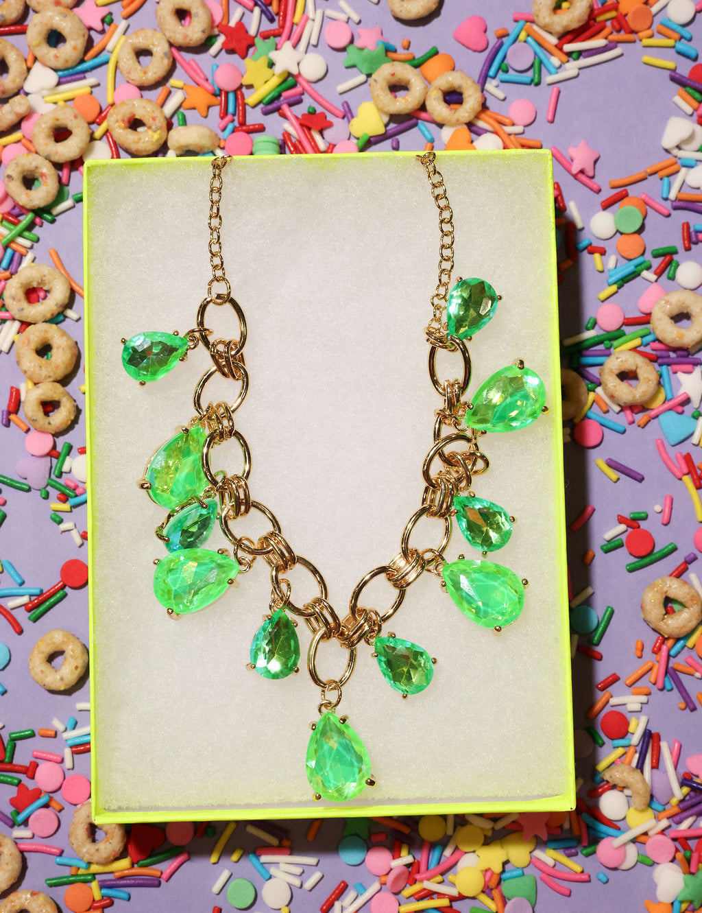 Necklace with green teardrop pendants on a yellow card surrounded by colorful cereal and sprinkles.