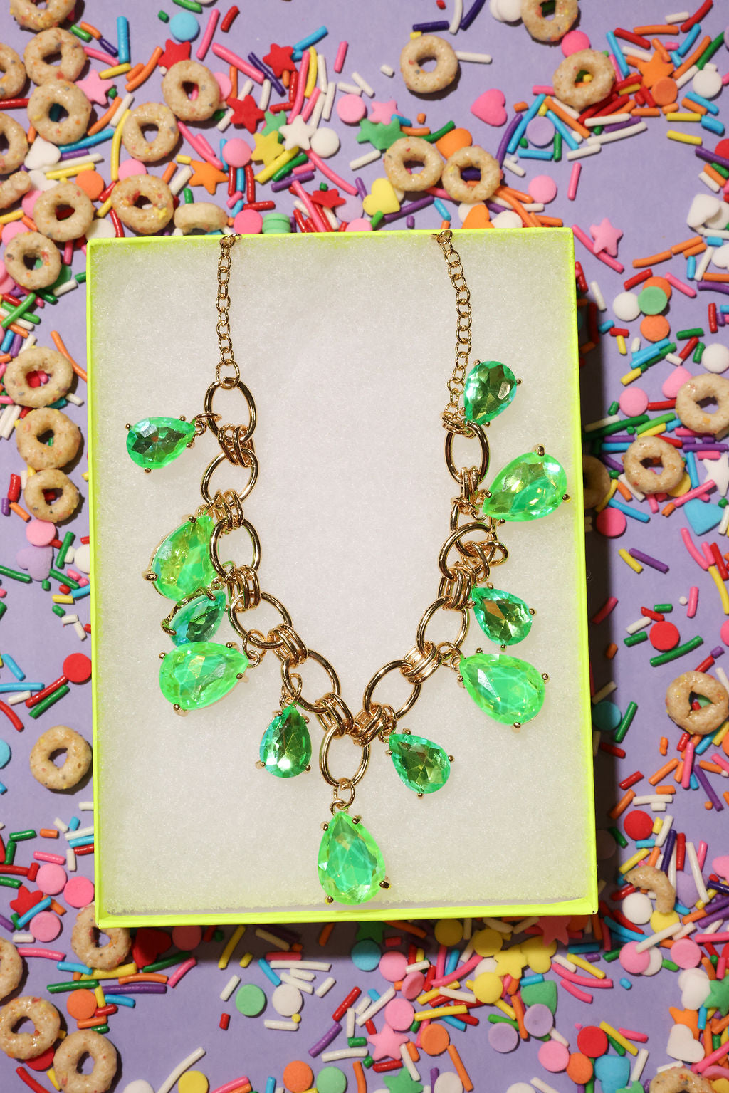 Necklace with green teardrop pendants on a yellow card surrounded by colorful cereal and sprinkles.