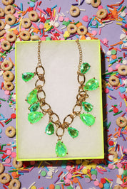 Necklace with green teardrop pendants on a yellow card surrounded by colorful cereal and sprinkles.