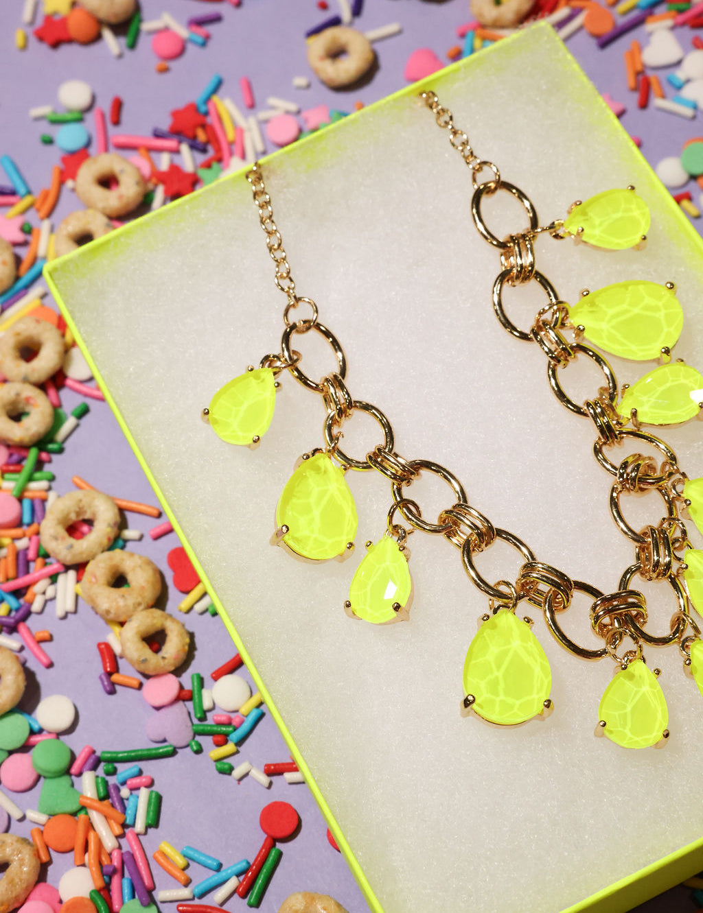 Neon yellow teardrop necklace on a colorful background with sprinkles and cereal.