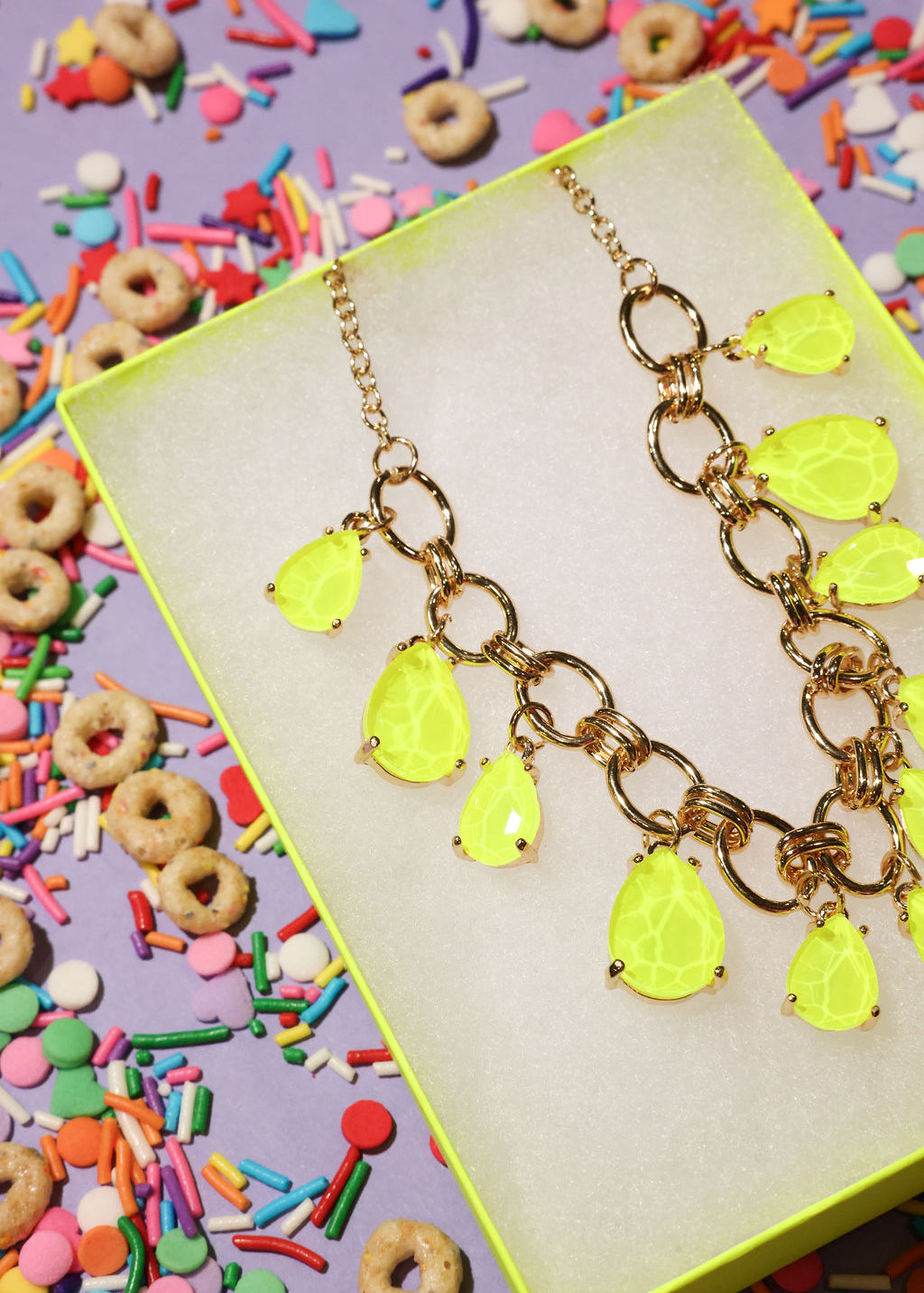 Neon yellow teardrop necklace on a colorful background with sprinkles and cereal.