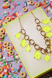 Neon yellow teardrop necklace on a colorful background with sprinkles and cereal.