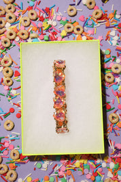 Colorful bracelet on a white card with a vibrant, multicolored background of donuts and sprinkles.